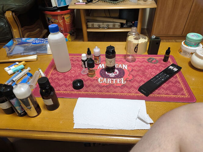 Diverses bouteilles d'e-liquide, des appareils de vapotage, une télécommande et des essuie-tout sont visibles sur un sous-verre rouge avec un texte sur une table en bois. (Légendé par l'IA)