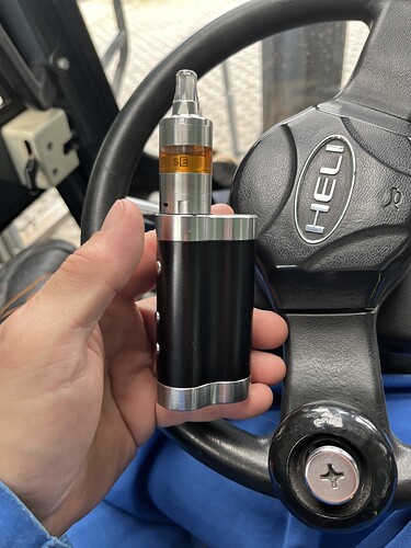 Une vape tenue dans une main est visible sur l'image, tandis qu'un volant de véhicule se trouve à l'arrière-plan. (Sous-titré par l'IA)