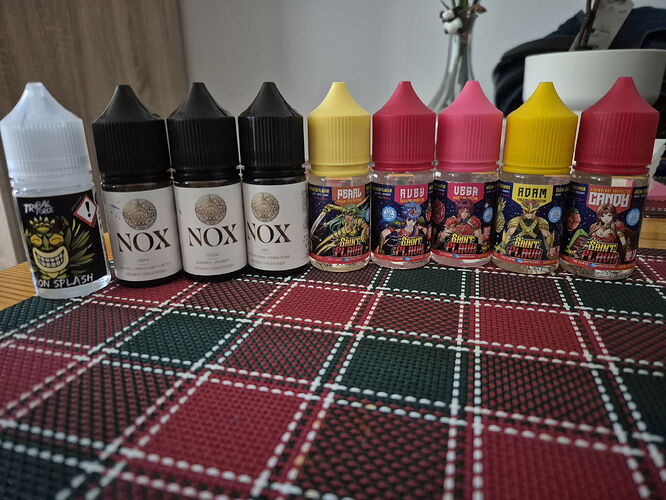 Plusieurs flacons d'e-liquide aux bouchons colorés sont alignés sur une nappe à motifs de Noël rouges et verts. (Étiqueté par IA)