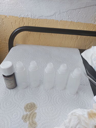 Az képen öt átlátszó üveg palack látható, amelyek egy asztalon sorakoznak, mellettük egy kisebb fekete üveg. (Feliratozva AI-val)