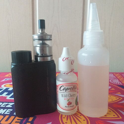 Sur la photo, un appareil utilisé pour le vapotage, une bouteille d'e-liquide et une bouteille de liquide saveur cerise sauvage sont visibles. (Légendé par IA)