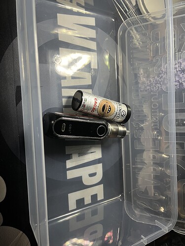 Az képen egy átlátszó tárolóedényben egy vape eszköz és egy üres ízesítésű folyadékpalack látható. (Feliratozva AI-val)