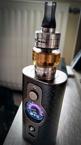 L'image montre un appareil de vapotage moderne avec un écran numérique sur le côté et un réservoir transparent rempli de liquide. (Légendé par IA)