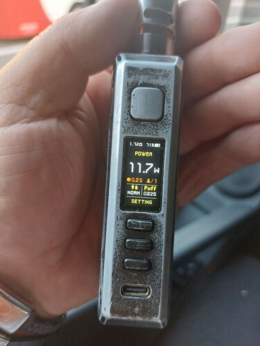 A hand holds a handheld electronic device with a screen and buttons, showing various technical data and settings. (Labeled by AI)