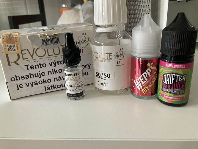 A variety of bottles and a box of Revolute branded e-liquid and vaping supplies are arranged on a white surface. (Subtitled by AI)