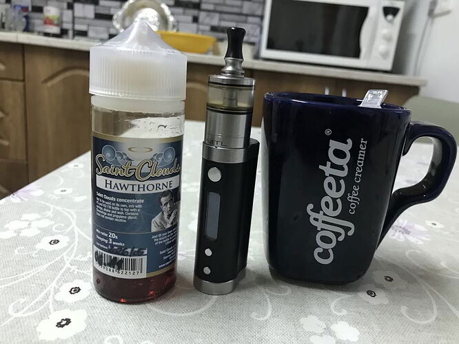 Sur la photo, une bouteille d'e-liquide, un vaporisateur et une tasse bleue sont visibles, avec l'inscription "coffeeta coffee creamer". (Légendé par IA)