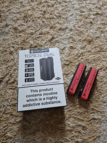 In the picture, a DOVPO TOPSIDE DUAL box and two red battery holders are visible on a carpet. (Labeled by AI)