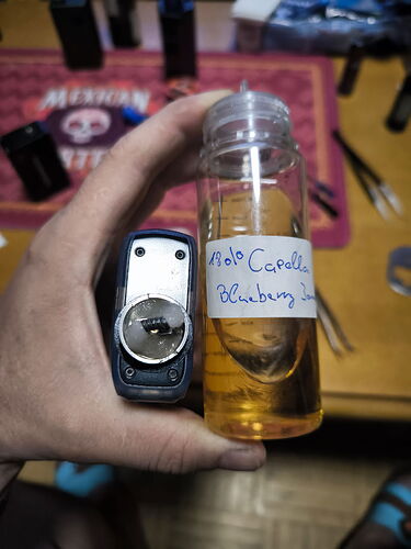 A hand holding two objects: an electronic lighter and a small plastic bottle filled with liquid, with a handwritten label. (Caption provided by AI)