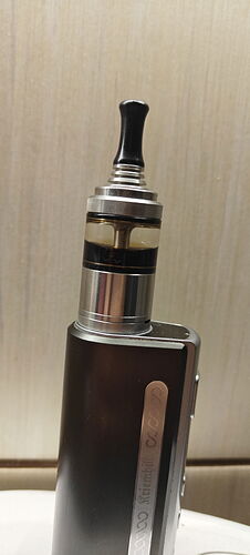 Az image egy fém elektromos cigaretta (vape) készüléket ábrázol fekete szájrésszel és átlátszó tartállyal. (Feliratozva AI-val)