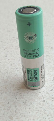 Egy zöld és ezüst színű, IMR 18650 típusú, 3500mAh kapacitású, 3,7V és 20A teljesítményű akkumulátor áll függőlegesen egy világos felületre téve. (Feliratozva AI-val)