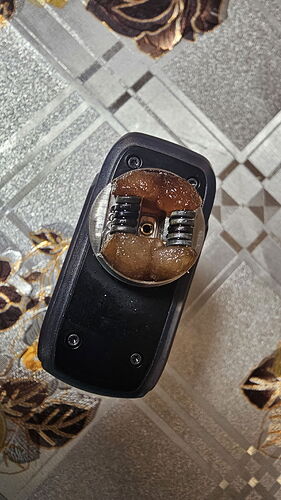 Egy elektronikusan működő eszköz, amelyen egy barna ragacsos anyag és két fém rugó látható. (Feliratozva AI-val)