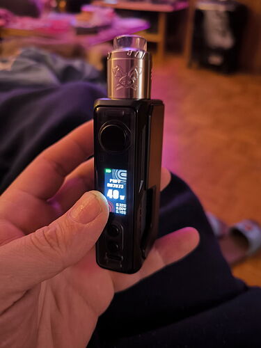 A vape device held in a hand, with a home environment in the background. (Chramed by AI)
