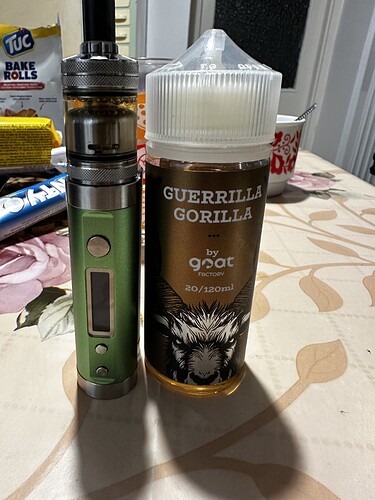 Un dispositif de vape vert est posé à côté d'une grande bouteille de e-liquide GUERRILLA GORILLA sur une table. (Légendé par IA)