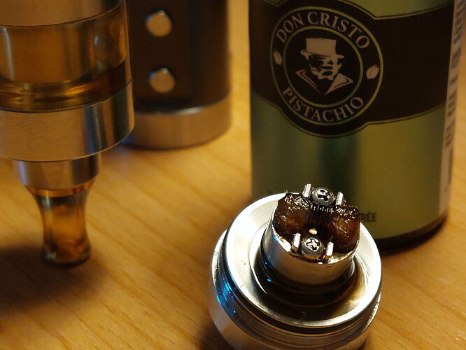 The picture shows a vape device, a part of it, and a bottle of e-liquid containing the "Don Cristo Pistachio" flavor. (Labeled by AI)