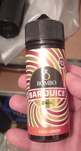 A hand holding a bottle of Bombo Bar Juice, containing cola lemon flavored liquid, in a quantity of 24 ml. (Labeled by AI)