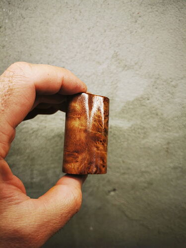 Une main tenant un petit cadre en bois chatoyant marron devant un mur à fond neutre. (Légendé par IA)