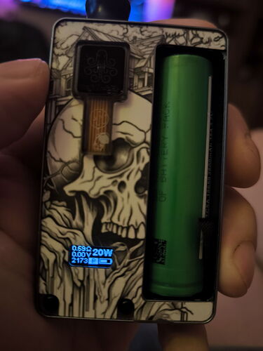 A képen egy kézzel tartott elektronikus dohányzó eszköz látható koponya mintával és zöld akkumulátorral. (Feliratozva AI-val)