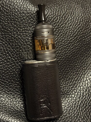 A képen egy fekete bőrtokba helyezett modern, fém és üveg vape cigaretta látható. (Feliratozva AI-val)