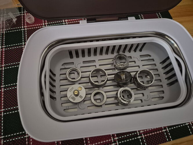 Az image egy ultrahangos tisztítókádot mutat, benne különböző fém alkatrészekkel. (Feliratozva AI-val)