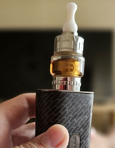 Egy kéz egy elektromos cigarettát (vape) tart, melyben barna színű folyadék látható. (Feliratozva AI-val)