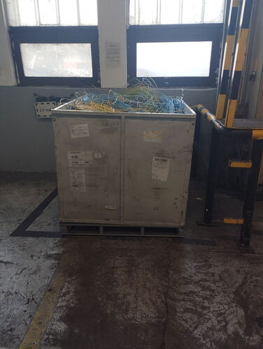 A large, metal storage bin sits on the floor of an industrial room, with colorful electrical wires on top. (Autotranscribed AI)