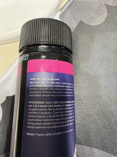 The image shows a black plastic bottle with a pink and black label on it, containing text in multiple languages. (Subtitled by AI)