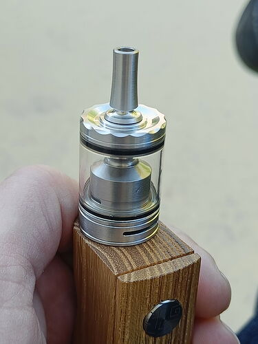 Une main tenant une cigarette électronique (vape) de type maison en bois devant un fond clair. (Légendé par IA)