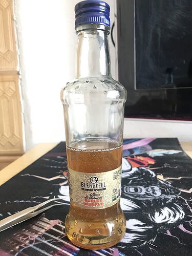 Une bouteille de soda en verre à moitié pleine avec un bouchon bleu est posée sur un sous-verre sombre et décoré. (Légendé par IA)