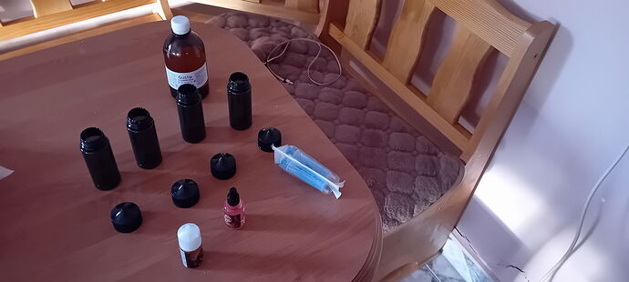 Various bottles and a syringe are visible on the table, while a wooden bench is in the background. (Subtitled by AI)