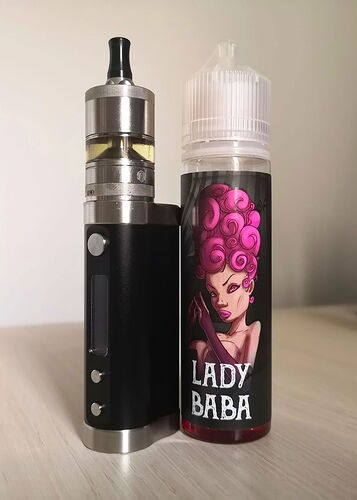 L'image montre une cigarette électronique noir argenté et à côté, un réservoir de liquide marqué "LADY BABA", représentant un personnage féminin aux cheveux roses. (Légendé par IA)