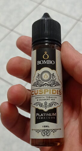 Une main tient une bouteille de 15 ml de e-liquide Bombo CUSPIDIS Platinum Tobaccos, contenant un mélange de tabac doux et de dessert. (Légendé par IA)