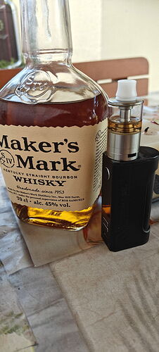 Une bouteille de whisky bourbon Maker's Mark et une cigarette électronique noire sont côte à côte sur une table. (Légendé par IA)