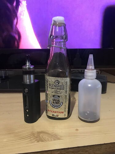 A black electronic cigarette, a bottle of liquid named Blendfeel Byzantium, and a plastic dropper bottle stand next to each other on the table. (Labeled by AI)