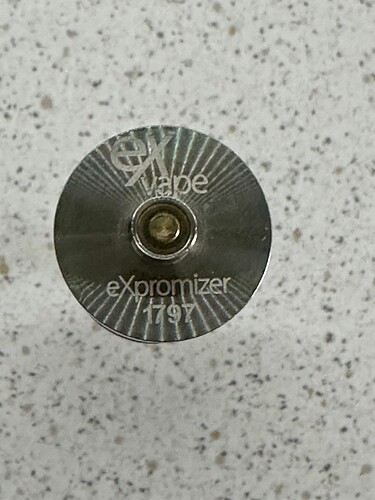 Az image egy e-cigaretta tartályának, az eXvape eXpromizer 1797-es modelljének a felülnézeti képe. (Feliratozva AI-val)