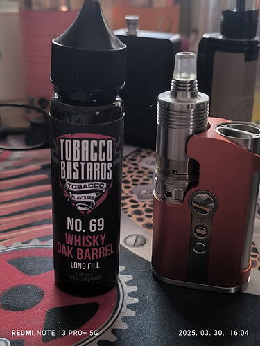 The image shows a "Tobacco Bastards" brand bottle of "Whisky Oak Barrel" flavored e-liquid and a vaporizer. (AI-generated caption)
