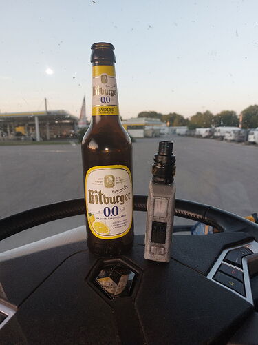 On the dashboard of the car, a Bitburger 0.0% alcohol-free beer and an e-cigarette stand in an open space. (Captioned by AI)