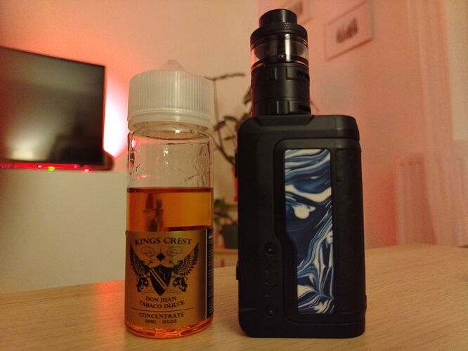 Un e-cigarette et une bouteille de concentré de marque Kinga Crest remplie de liquide sont visibles sur la table. (Sous-titré par IA)