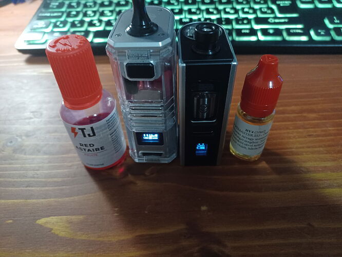 Az asztalon lévő e-cigaretták és liquid palackok láthatók, háttérben világító billentyűzettel. (Feliratozva AI-val)