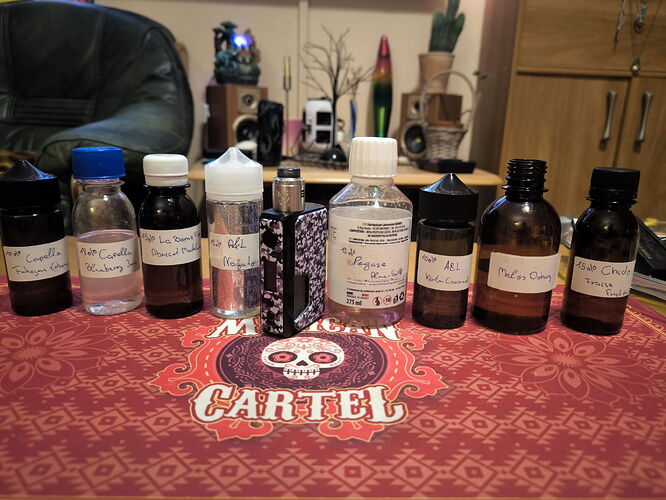 On the table are various small bottles and an e-cigarette on a red tablecloth with the inscription "Cartel". (Caption by AI)