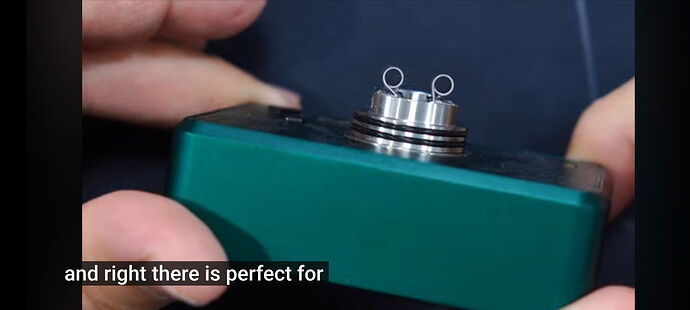 A green device is held, featuring a metal coil with two small loops. (Captioned by AI)