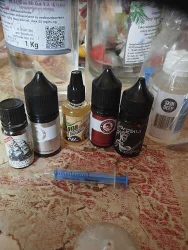 Az asztalon öt különböző méretű és címkéjű műanyag palack, valamint egy kék színű fecskendő látható. (Feliratozva AI-val)