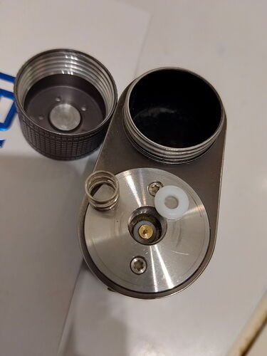 Az ábrán egy szétválasztott fém eszköz látható, amely különféle alkatrészekből áll, beleértve a csavart kupakot és az alsó részen elhelyezkedő fém részeit. (Feliratozva AI-val)