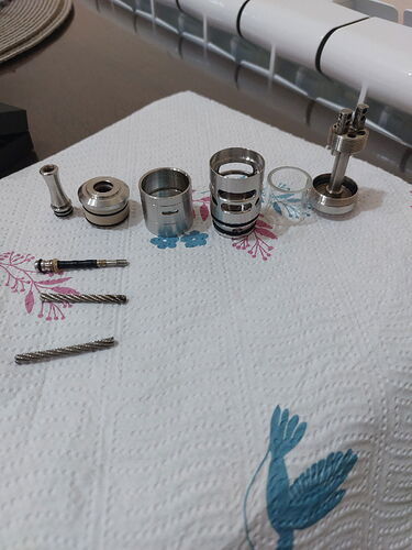 L'image montre diverses pièces métalliques et vis placées sur une surface textile blanche à motifs. (Légendé par l'IA)