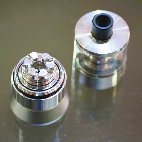 Az изображение egy fém és üveg anyagú vaper tartály részleteit mutatja, amely a nikotinos gőz előállításához szükséges. (Feliratozva AI-val)