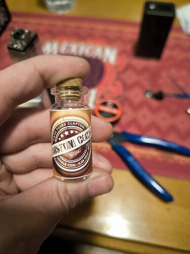 A képen egy kis üvegcse látható, amelyben valószínűleg ízesítéshez használt folyadék található, miközben egy asztalon eszközök és tartozékok is láthatók. (Feliratozva AI-val)