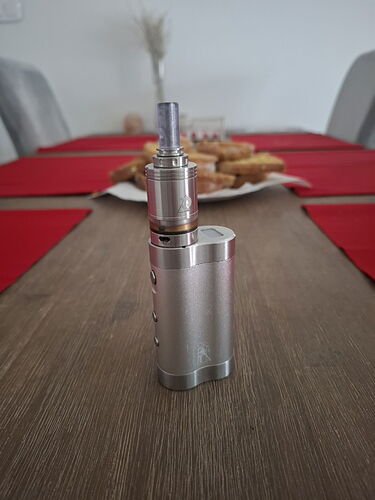 A metal electronic cigarette (vape) stands on the table, with a bowl of cake and red napkins visible behind it. (Labeled by AI)
