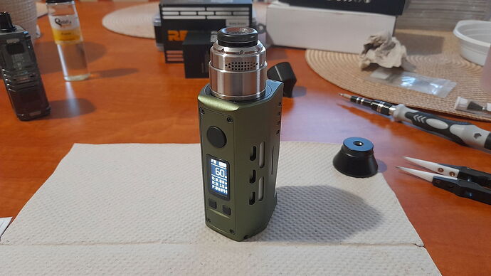 A green vape device stands on a paper towel on a table, surrounded by various tools and boxes. (Subtitled by AI)