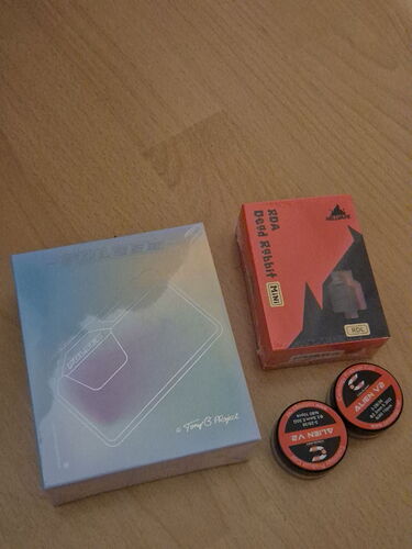 Az asztalon egy PlayStation 5 konzol doboza, egy piros és fekete PlayStation Digital Edition doboz, valamint két kis, kerek tartály található. (Feliratozva AI-val)