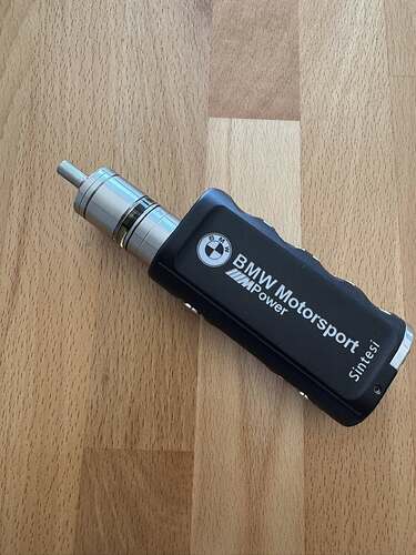 Cette image représente un appareil de vapotage moderne orné d'un logo BMW Motorsport, fabriqué à partir d'éléments métalliques et plastiques. (Légendé par l'IA)