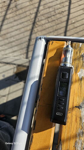 Un appareil de vapotage noir posé sur un banc en bois, au soleil. (Sous-titré par IA)